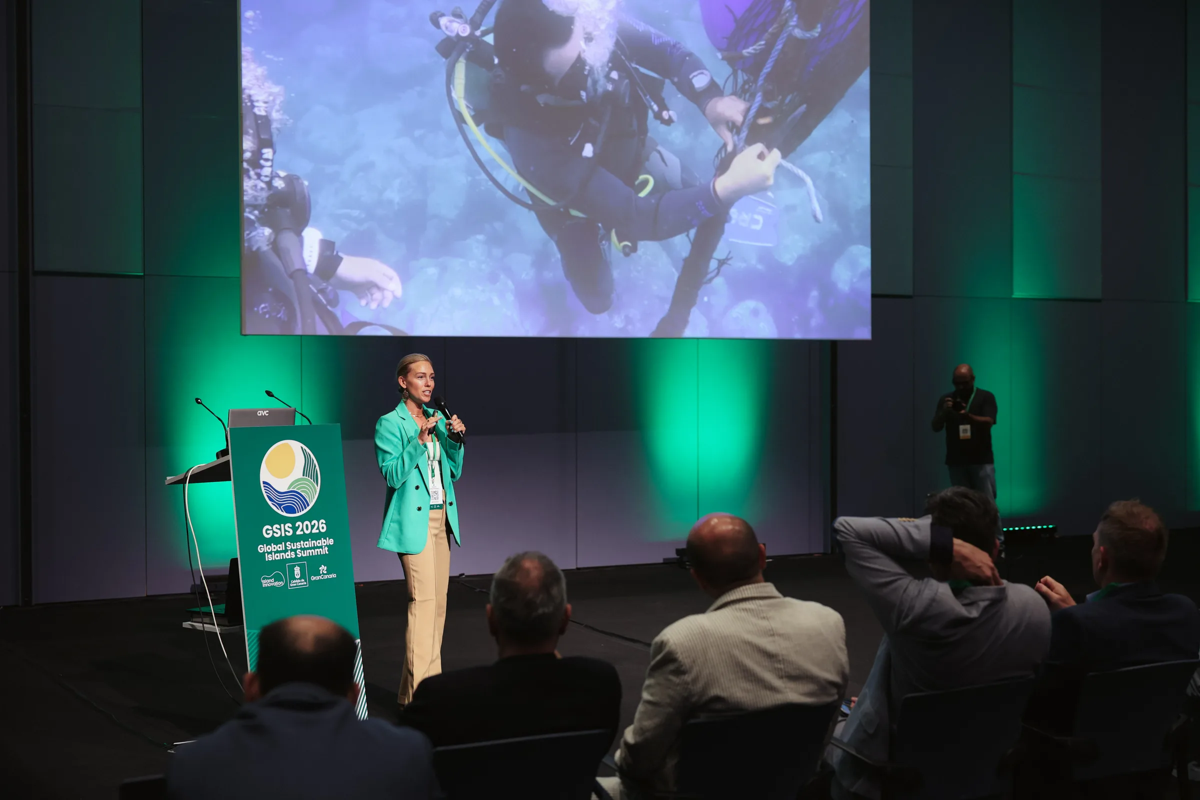 A speaker presents on stage beneath a large ocean-cleanup image, with the GSIS 2026 Global Sustainable Islands Summit banner and a seated audience in the foreground, Solutions Showcase, Gran Canaria